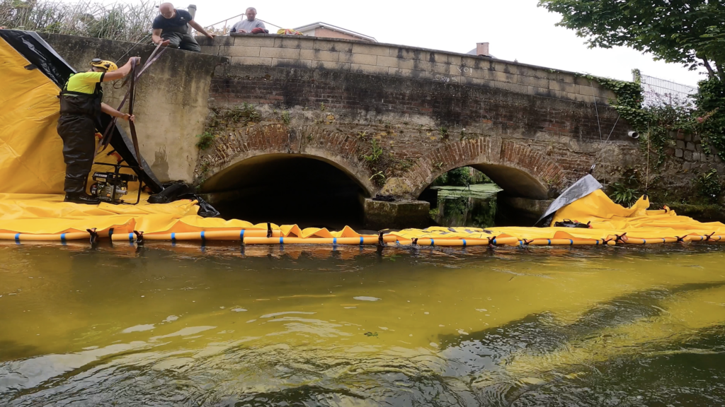 Équipe installant un batardeau souple Water-Gate© devant un pont sur la Valmont à Fécamp.