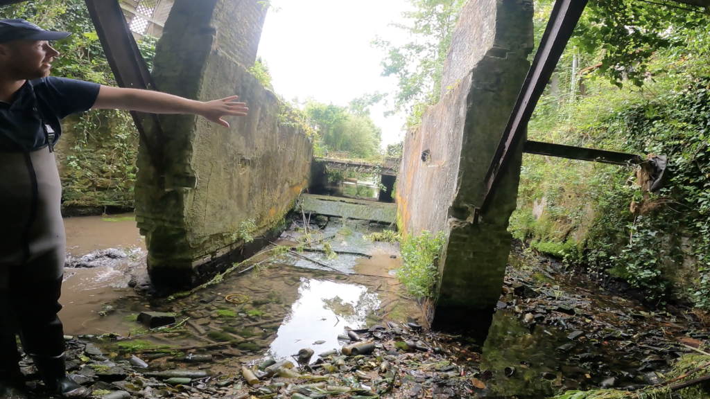 Ancien ouvrage hydraulique asséché sur la Valmont à Fécamp avec déchets en verre présents dans le lit du cours d’eau avant travaux de restauration écologique.